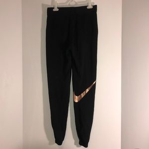 Black Nike sweatpants with large rose gold symbol.